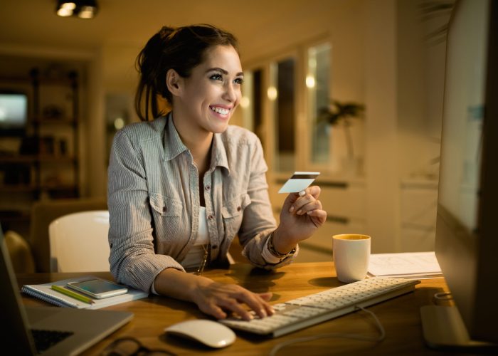 Happy woman using credit card for online banking at night at hom Young happy woman using credit card for online shopping in the evening at home.